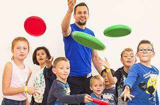 Viele Kinder haben Spaß beim Frisbee Spielen mit einem Coach.